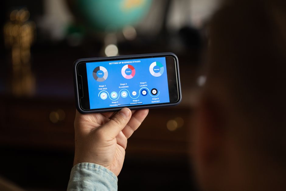 A person holds a smartphone displaying business strategy stages chart indoors.